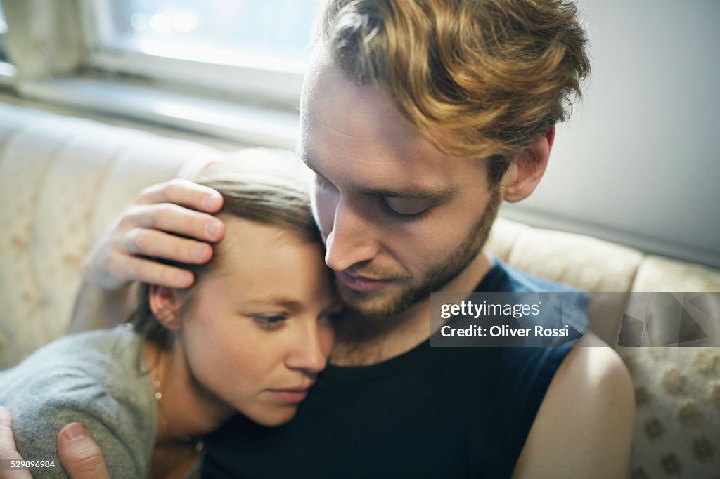 Young man hugging serious woman on couch