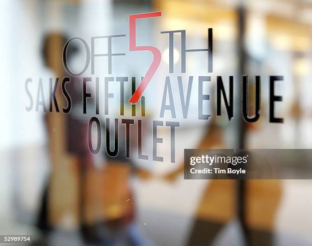 Hand-holding couple is reflected in signage for Off 5th Saks Fifth Avenue Outlet store at Old Orchard shopping center May 27, 2005 in Skokie,...