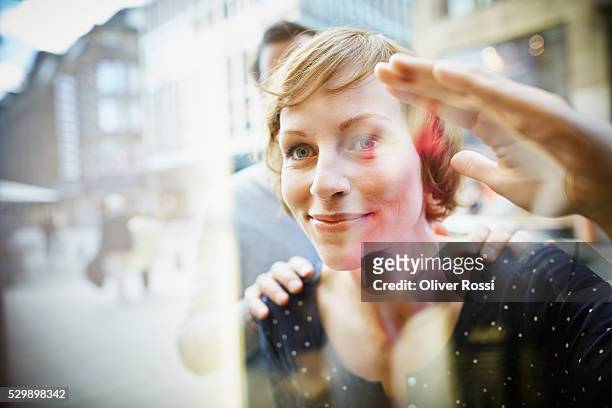 smiling couple behind window - window shopping stock-fotos und bilder