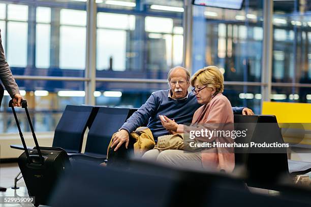 senior couple using smart phone at airport - airport couple stock-fotos und bilder