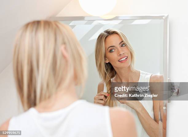 beautiful blonde doing her hair in front of mirror - tressé photos et images de collection