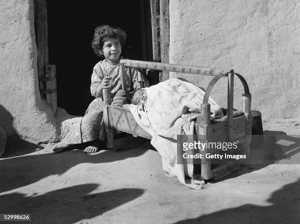 Three months after Israel's first occupation of this war-torn area, an Arab girl rocks her baby brother to sleep February 1, 1957 in Beit Hanun in...