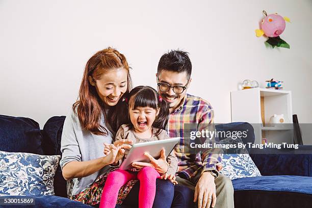 happy family using tablet joyfully at home - three people on couch stock pictures, royalty-free photos & images