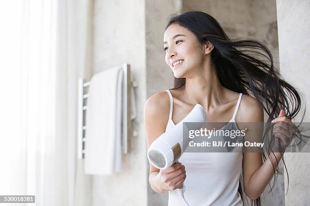 young woman drying her hair with a hair dryer - asian hair stock-fotos und bilder