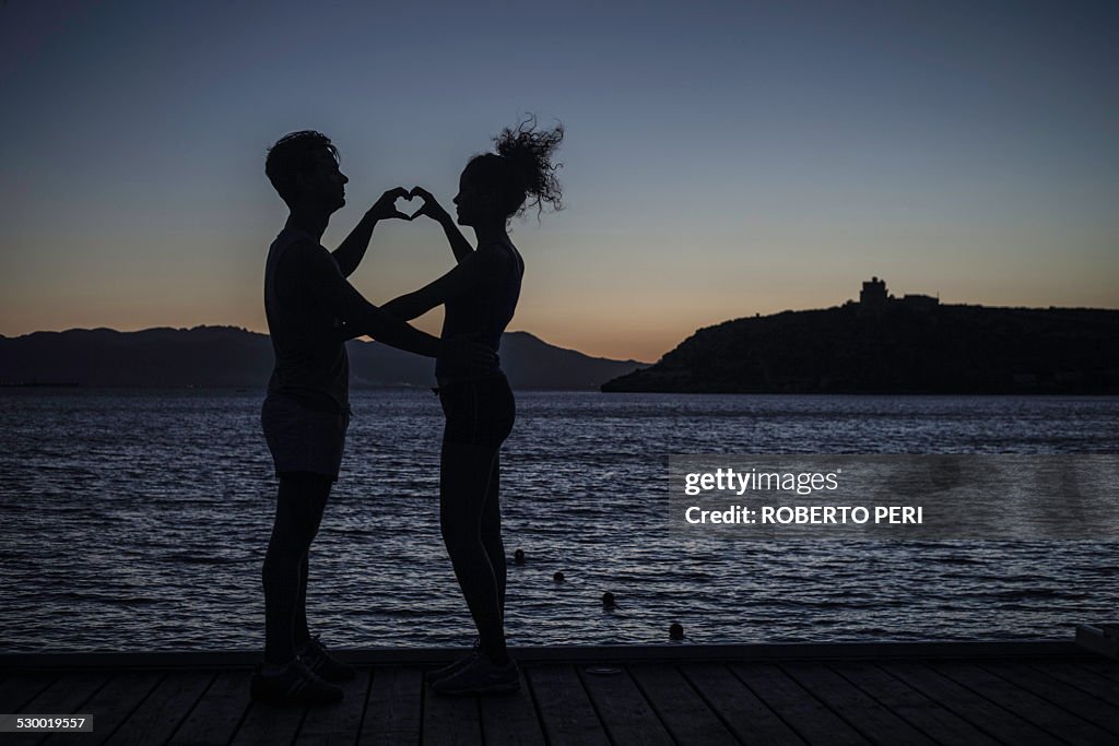 Couple making heart shape with hands by sea, silhouette