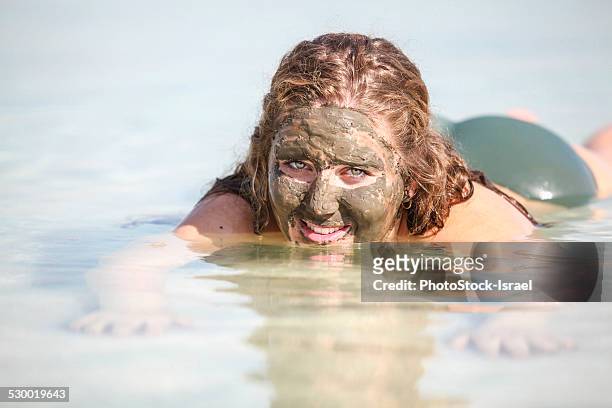 mud covered female tourist floats in the dead sea, israel - dead sea float stock pictures, royalty-free photos & images