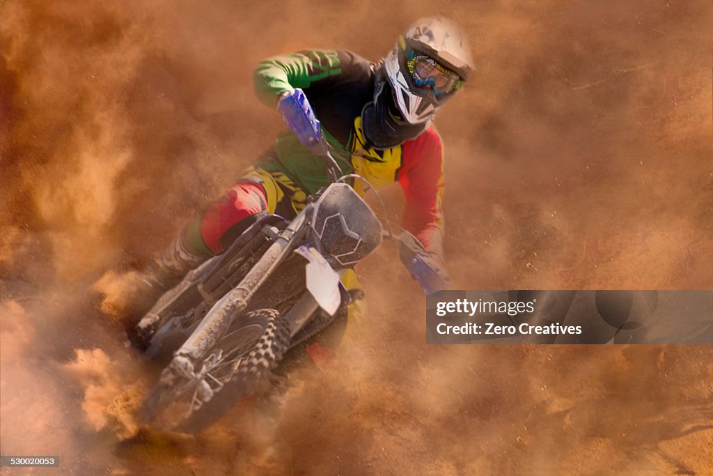 Young male motocross rider racing in dust