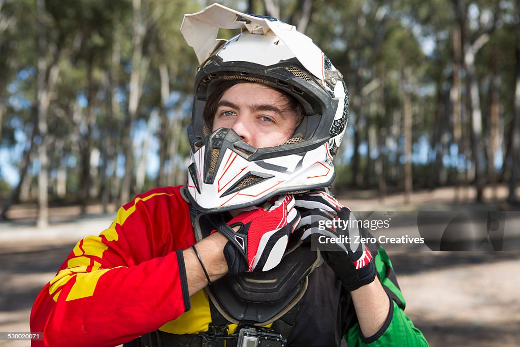 Motocross motorcycle competitor fastening helmet in forest