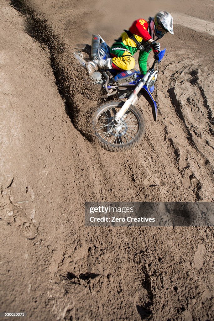 Young male motocross rider racing down mud hill