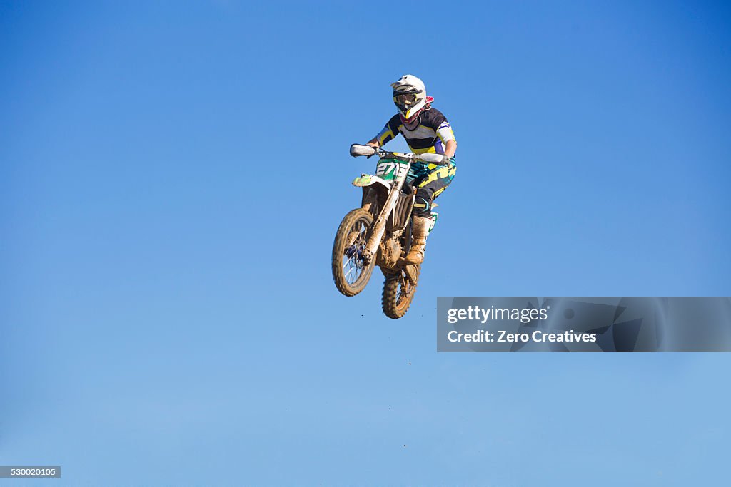 Young male motocross racer jumping mid air against blue sky