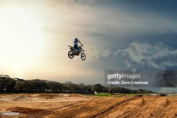 silhouetted young male motocross racer jumping mid air over mud track - motorcycle stunt stock pictures, royalty-free photos & images