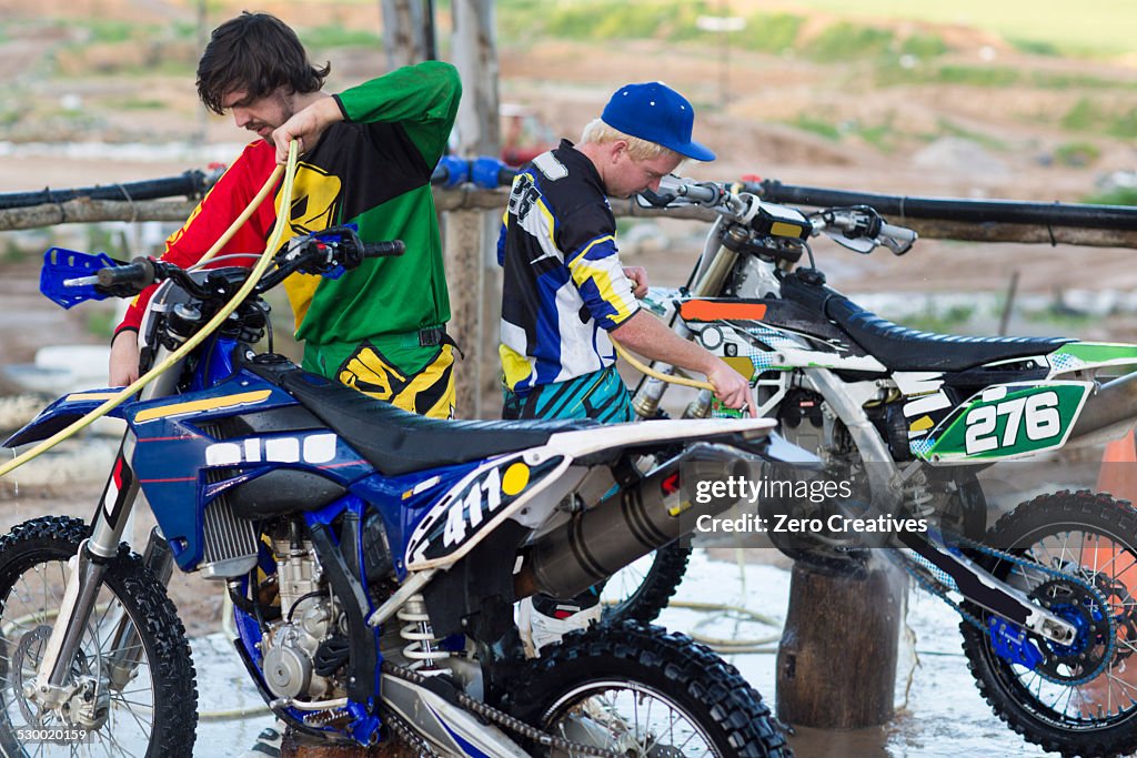 Two male motocross competitors cleaning motorcycles with water hoses