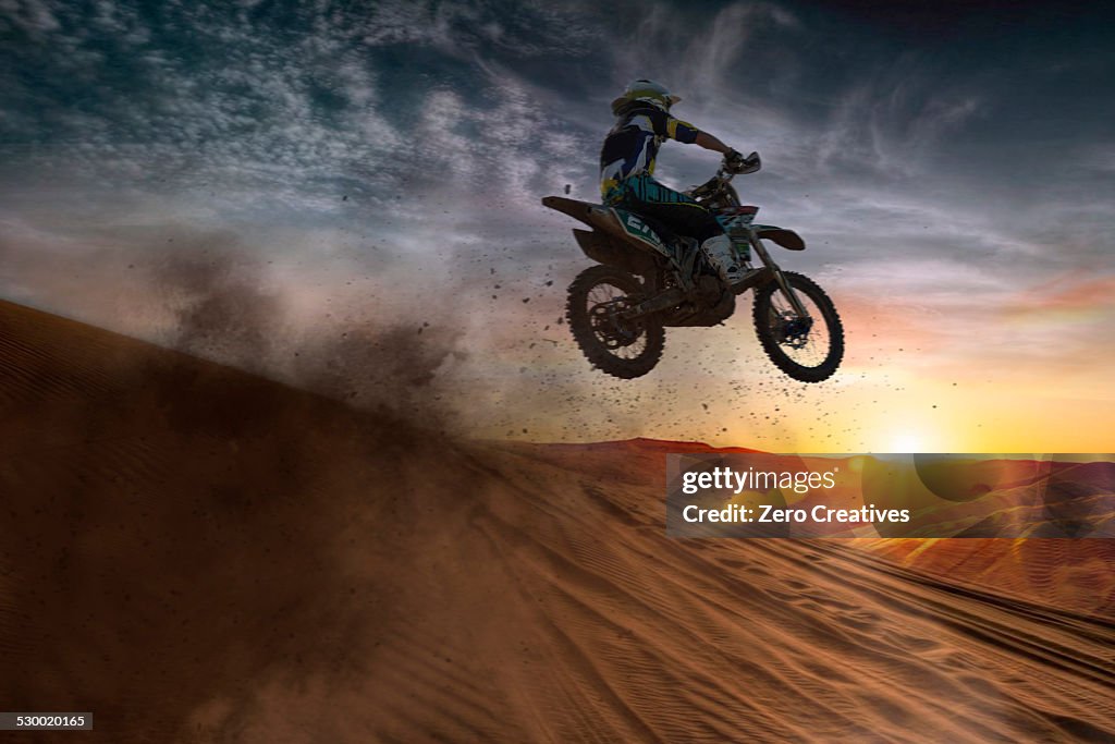 Young male motocross racer jumping mid air at sunset