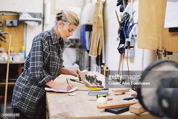 Young craftswoman making notes at workbench in pipe organ workshop