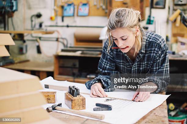 young craftswoman measuring blueprint on workbench in pipe organ workshop - handgemacht stock-fotos und bilder
