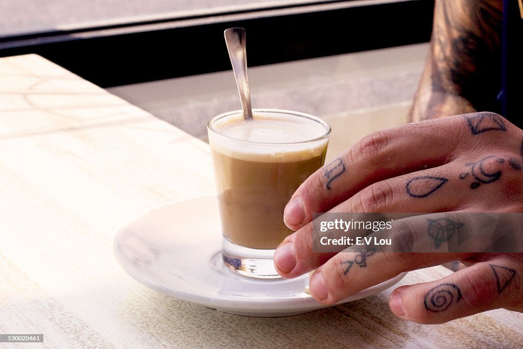 Tattooed hand of young man and coffee shotglass on cafe table