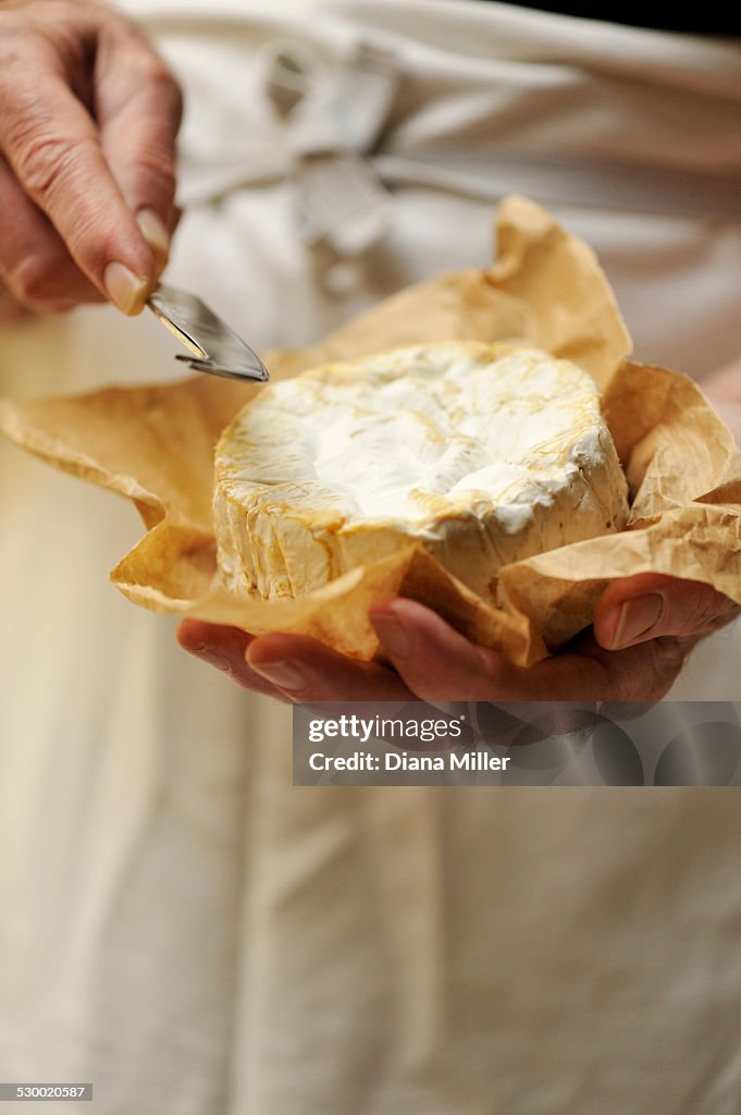 Man holding goats cheese and cheese knife, focus on hands