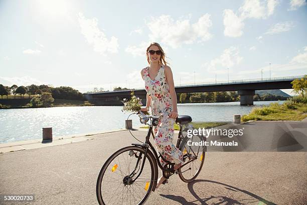 young woman cycling along riverside, danube island, vienna, austria - summer frock stock pictures, royalty-free photos & images