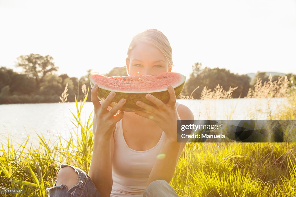 Portrait of young woman holding up melon slice in front of face, Danube Island, Vienna, Austria
