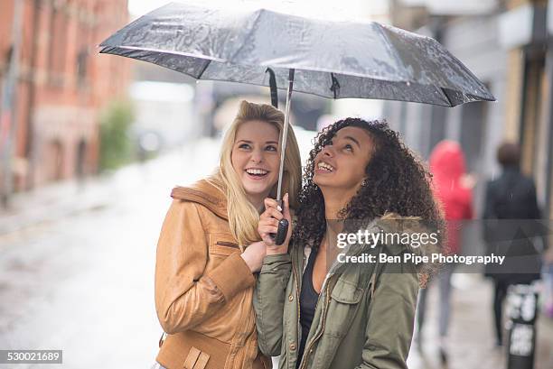 young women sheltering under umbrella - raining umbrella stock pictures, royalty-free photos & images