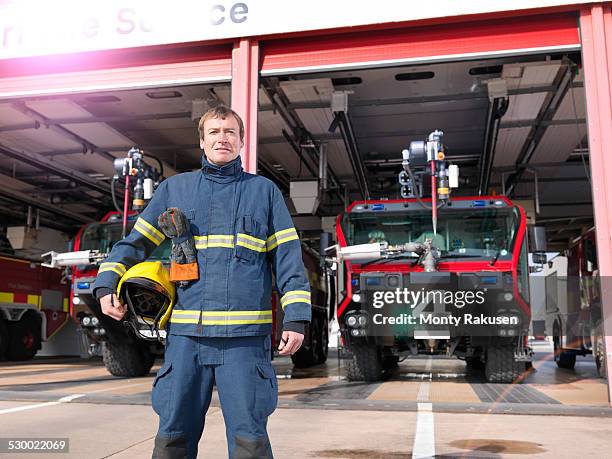 portrait of fireman in front of fire engines in airport fire station - fireman uk stock pictures, royalty-free photos & images