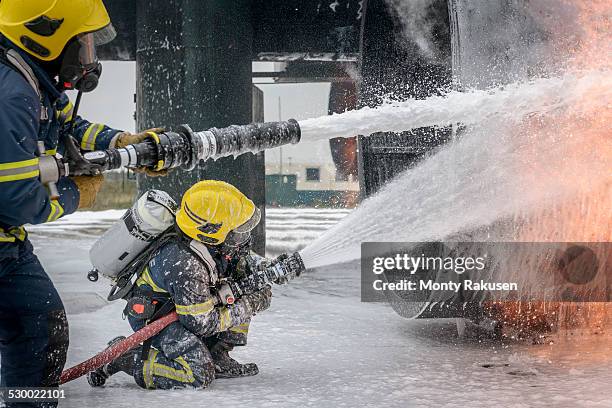 firemen spraying water on simulated aircraft fire at training facility - feuerwehrschlauch stock-fotos und bilder