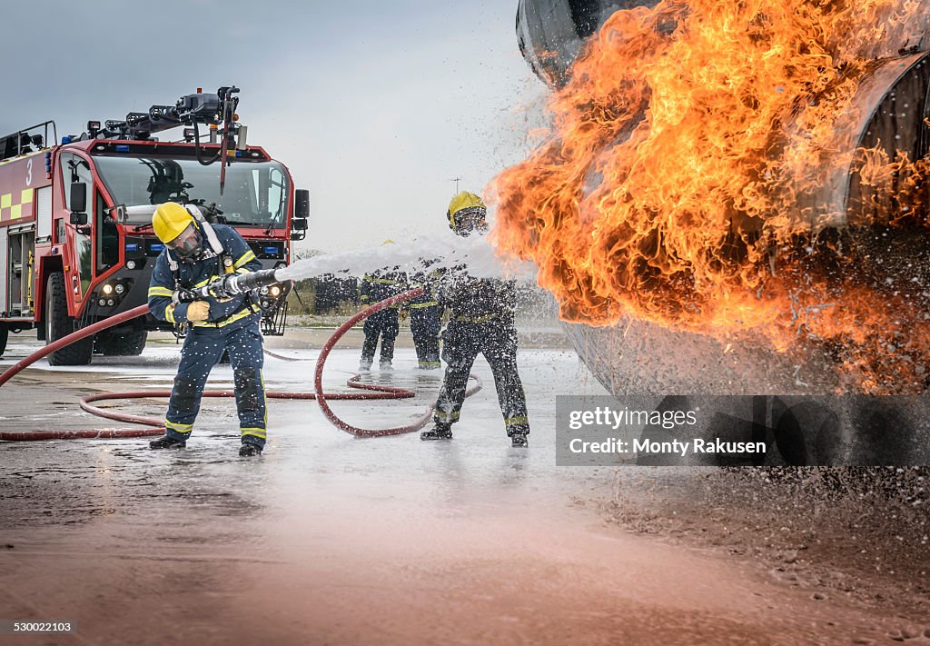 Firemen spraying water on simulated aircraft fire at training facility