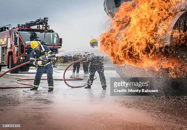 firemen spraying water on simulated aircraft fire at training facility - brandslang stockfoto's en -beelden