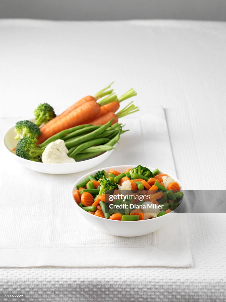 Raw vegetables in bowl with bowl of boiled vegetables