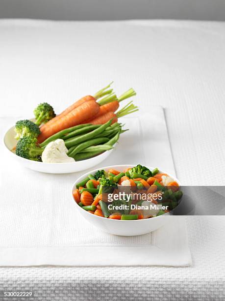 raw vegetables in bowl with bowl of boiled vegetables - ベビーキャロット ストックフォトと画像