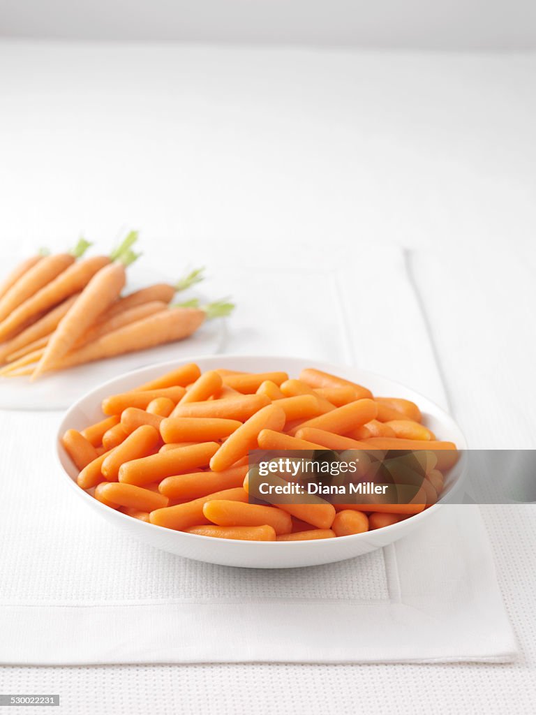 Raw carrots on marble cutting board and bowl of boiled carrots