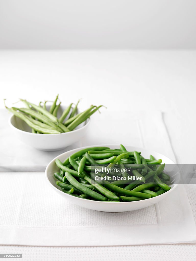 Raw green beans in bowl on cutting board and bowl of boiled green beans