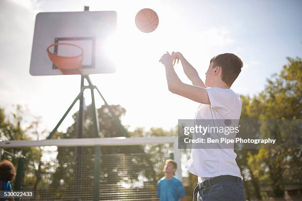 young male basketball player throwing basketball into hoop - bethnal green fotografías e imágenes de stock