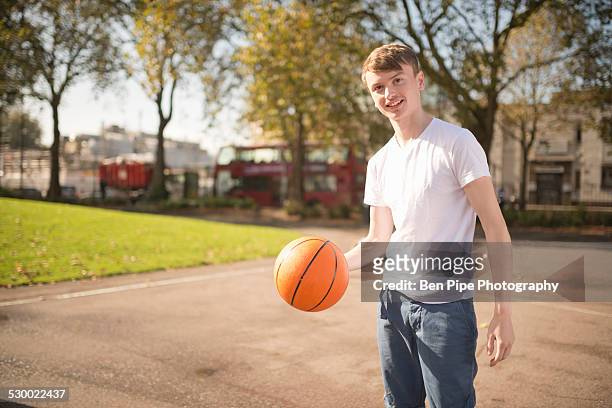 portrait of smiling young male basketball player holding basketball - one teenage boy only fotografías e imágenes de stock