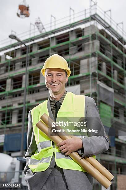 portrait of a happy male site manager standing with blueprints at a construction site, bavaria, germany - architekt mit plan frontal stock-fotos und bilder