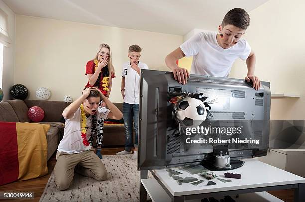 teenage soccer fans in living room with ball demolishing tv - broken tv stock-fotos und bilder