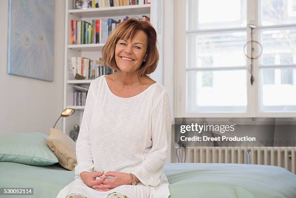 senior woman sitting on bed and smiling, munich, bavaria, germany - old lady nightgown stock pictures, royalty-free photos & images