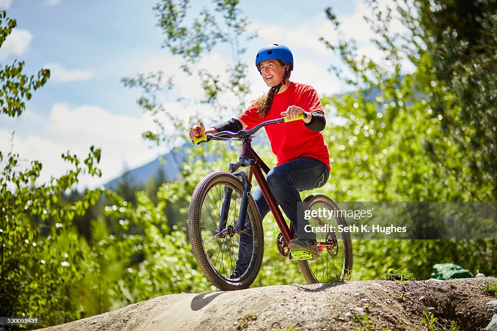 Young female bmx biker poised on edge of rock in forest