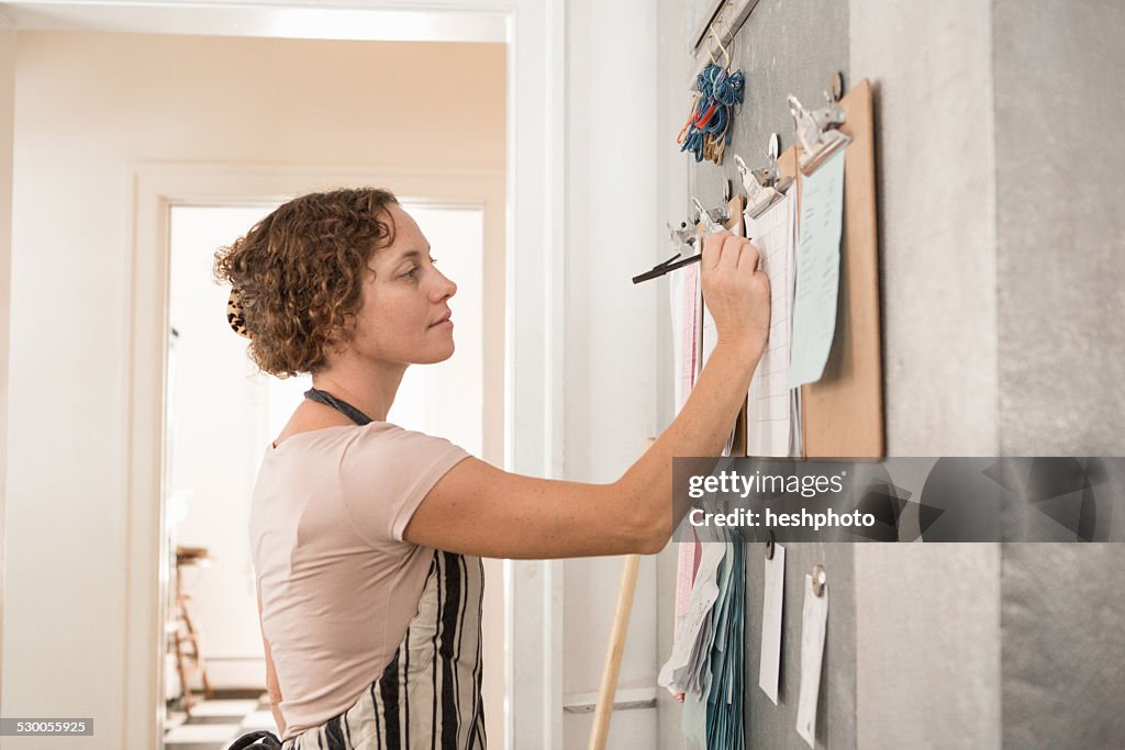 Female shop assistant writing on wall clipboards in kitchen at country store