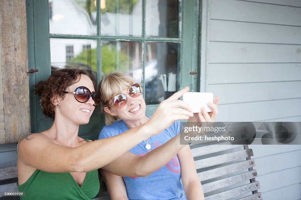 Two mid adult woman taking smartphone selfie on porch