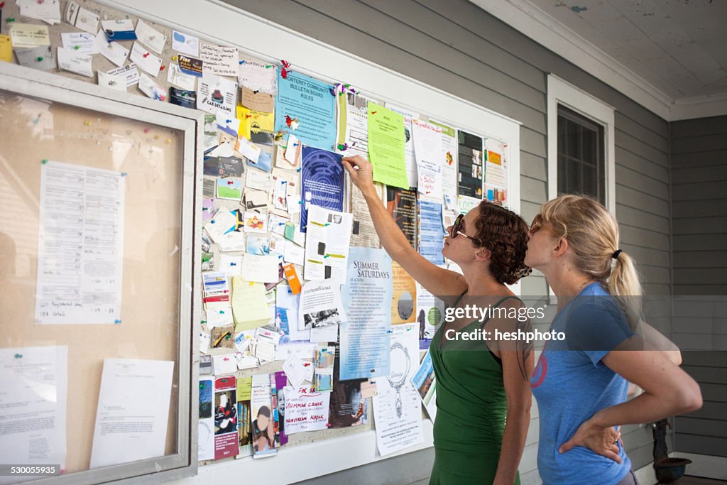 Two mid adult women looking up at community notice board