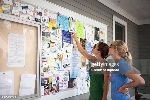 two mid adult women looking up at community notice board - heshphoto - fotografias e filmes do acervo