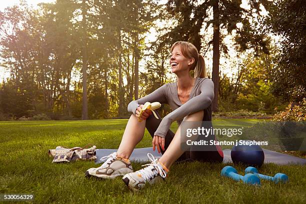 mid adult woman sitting in park taking exercise break - banane essen stock-fotos und bilder