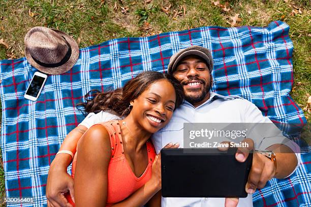 couple lying on grass watching movie on tablet - couple travel tablet stock-fotos und bilder