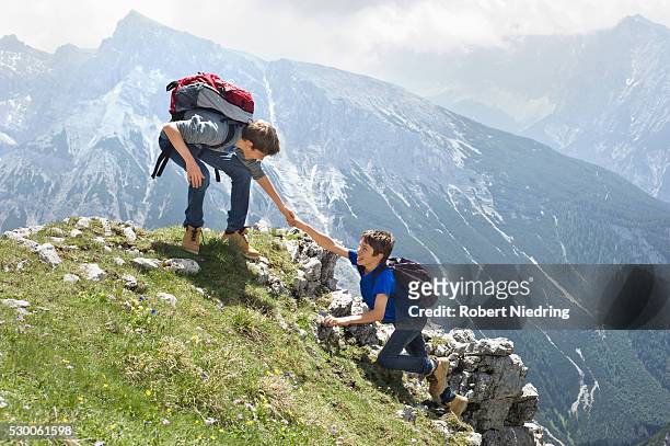 teenage boys helping friend climbing in mountains - hiking across the karwendel mountain range stock pictures, royalty-free photos & images
