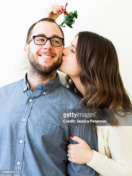woman kissing man under mistletoe - mistel stock-fotos und bilder