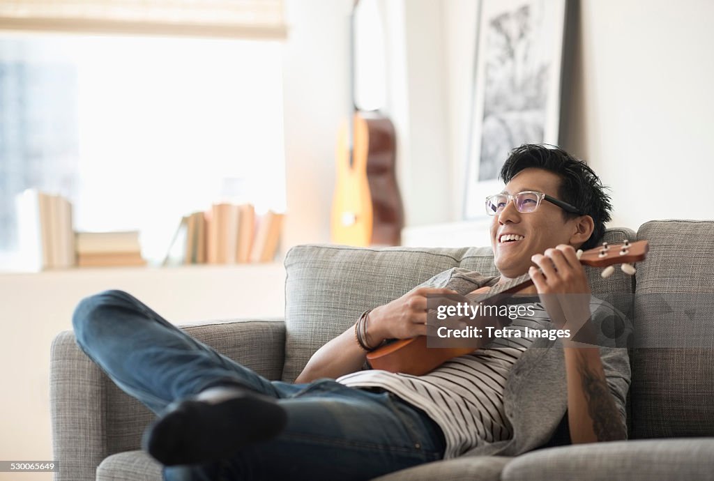 USA, New Jersey, Jersey City, Man sitting on sofa and playing ukulele