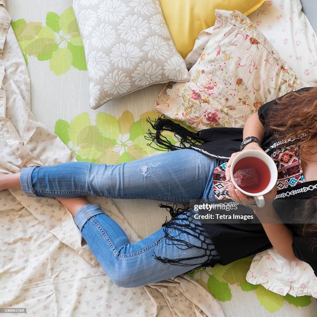 USA, New Jersey, Jersey City, Woman lying down on bed with tea cup