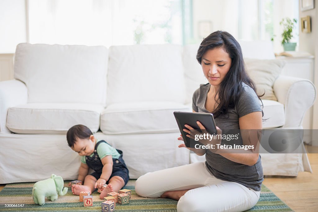 USA, New Jersey, Jersey City, Mother using tablet pc while her son (6-11 months) playing with building blocks