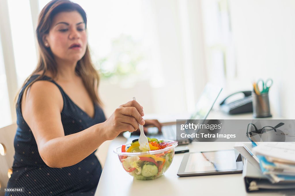 USA, New Jersey, Jersey City, Woman eating salad and using laptop in office